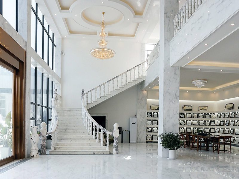 The showroom: a white marble staircase with carved balusters, chandeliers, and a wall of framed mosaic samples